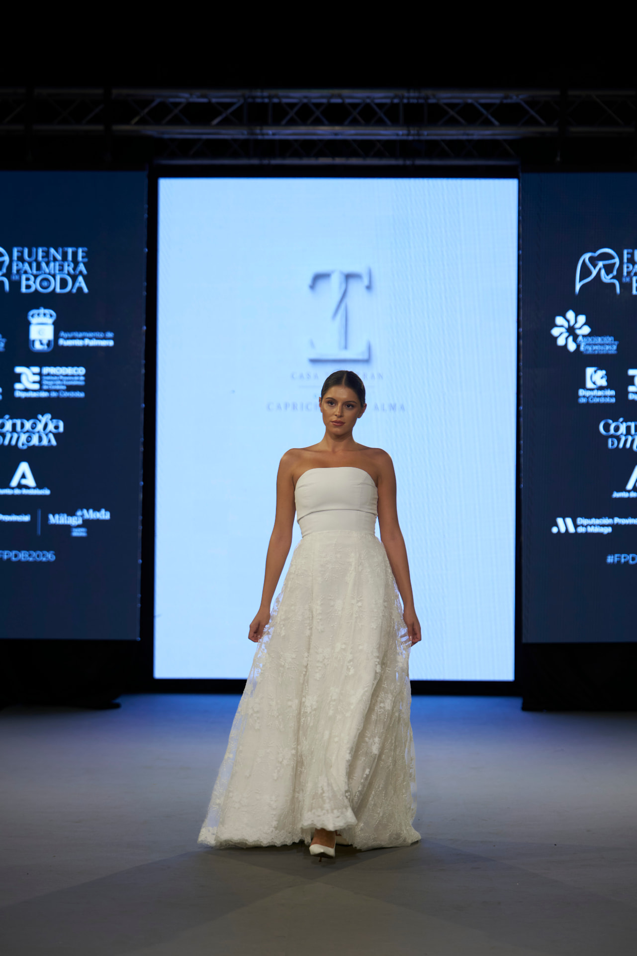 Vestido de novia palabra de honor con falda de encaje floral, de frente ante la pantalla de la colección