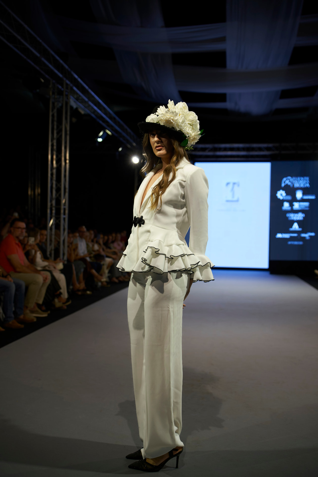 Traje de chaqueta blanco con volantes y sombrero floral, de perfil