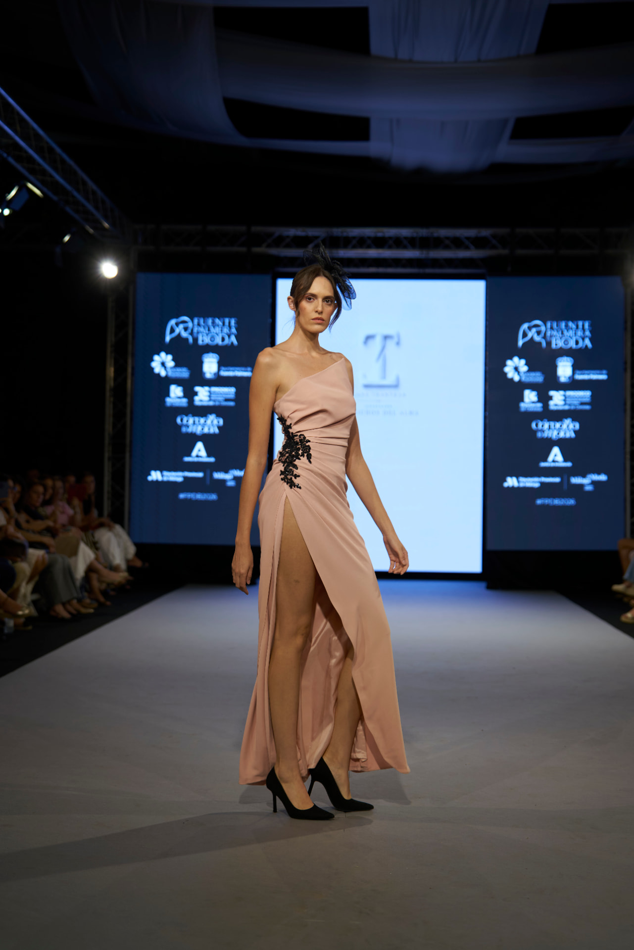 Vestido largo rosa empolvado con bordado negro lateral y tocado de plumas, de frente