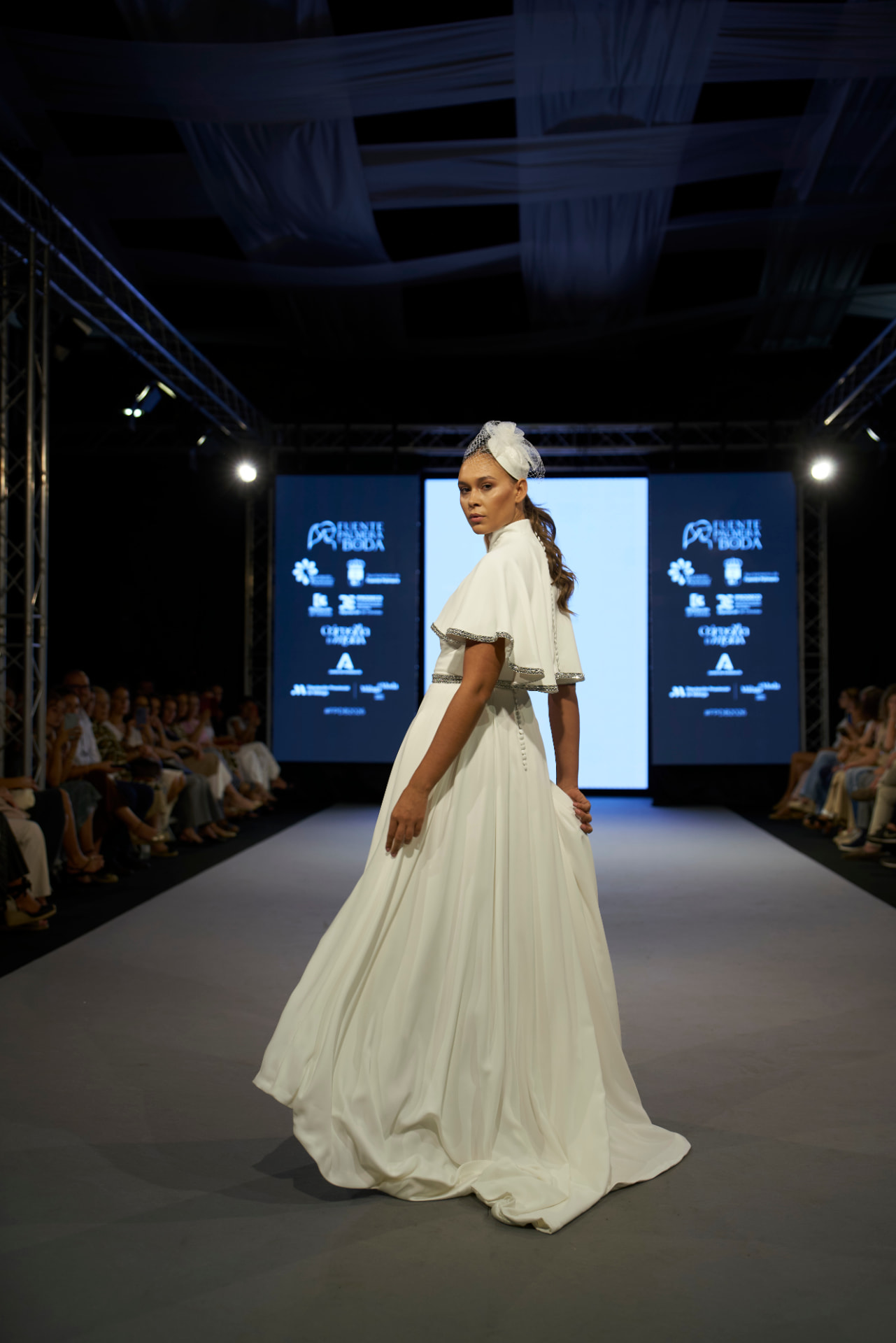 Vestido de novia con capa corta y tocado, girando en la pasarela