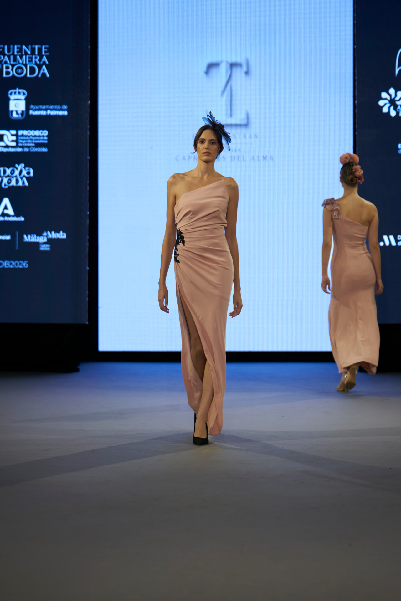 Traje largo rosa palo drapeado con abertura y aplique negro, con tocado de plumas oscuras, de frente