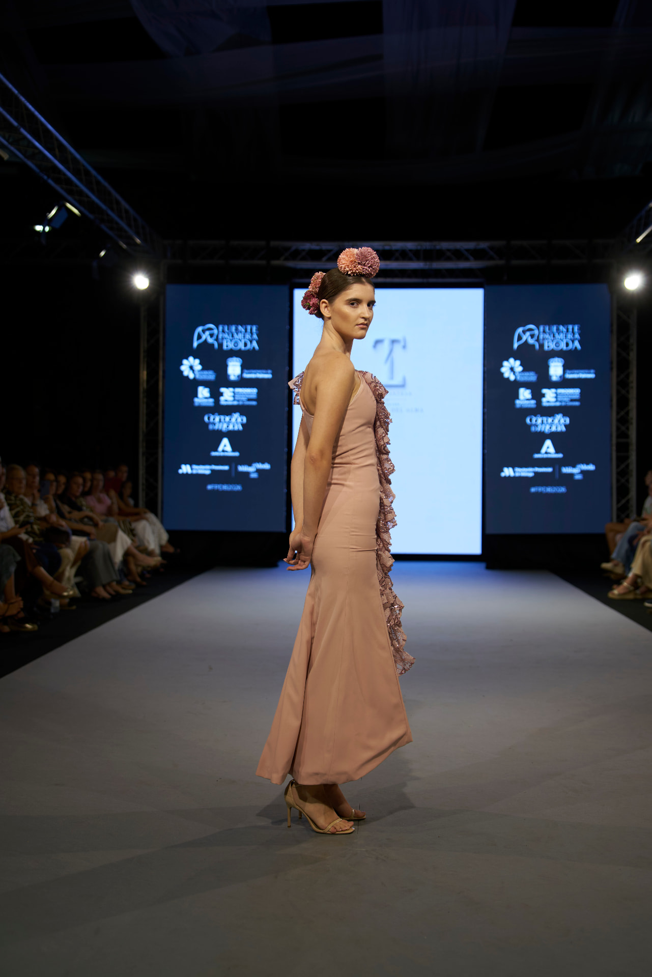 Vestido largo rosa empolvado de tejido fluido con tocado de flores, posando de perfil