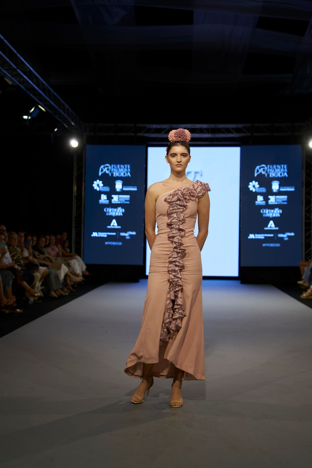 Vestido rosa de un hombro con volante de lentejuelas y tocado floral, de frente