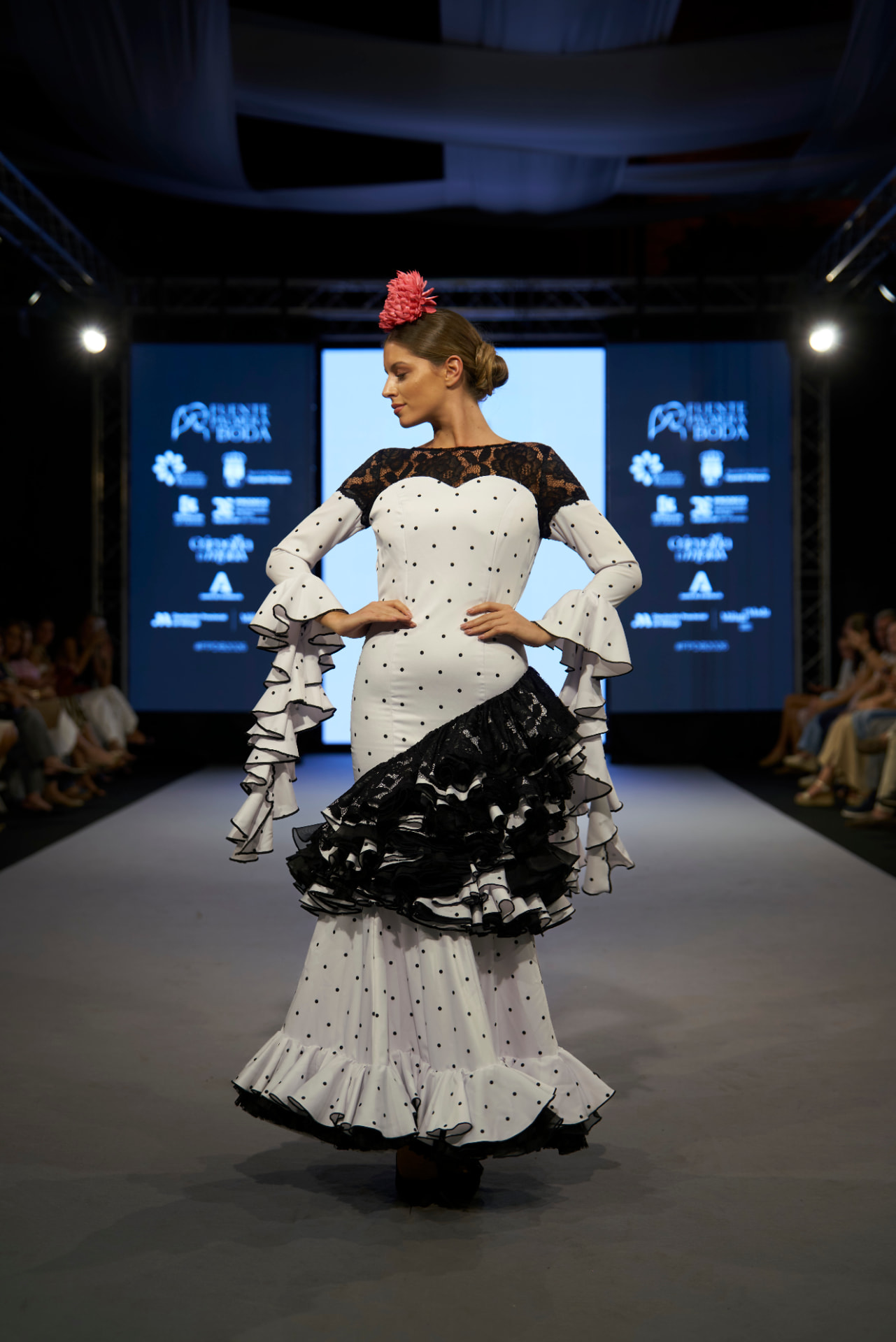 Traje de flamenca blanco de lunares con encaje negro y volantes asimétricos, manos en la cintura