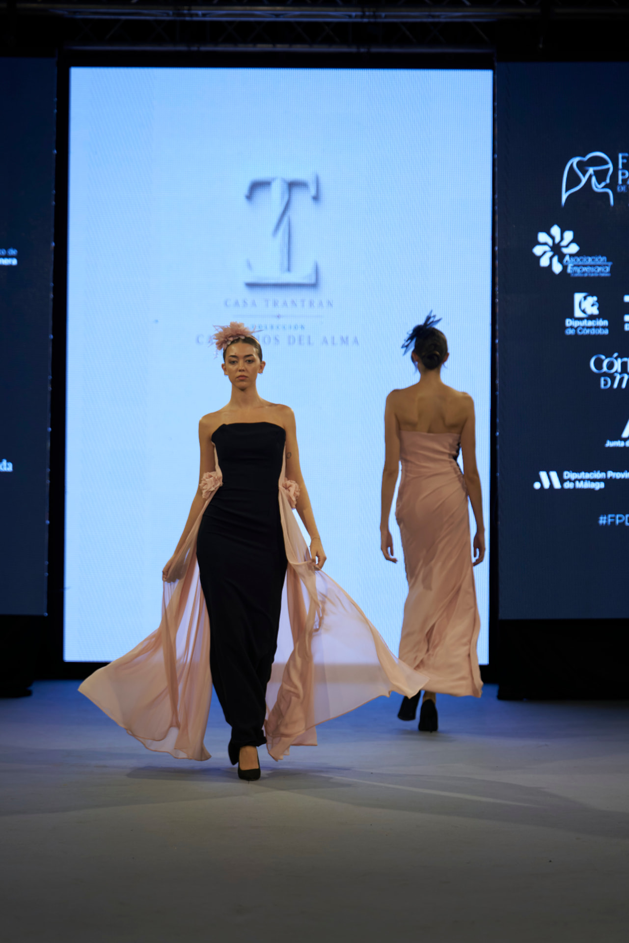 Vestido negro columna con caídas de gasa rosa y tocado de plumas, de frente