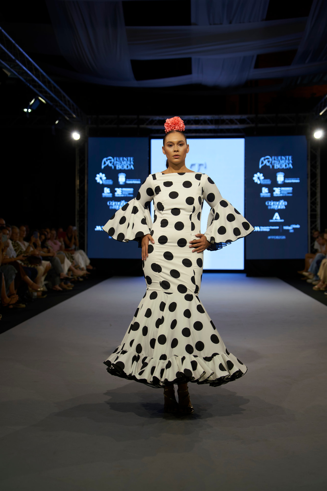 Traje de flamenca blanco de lunares negros con volantes y flor coral, de frente