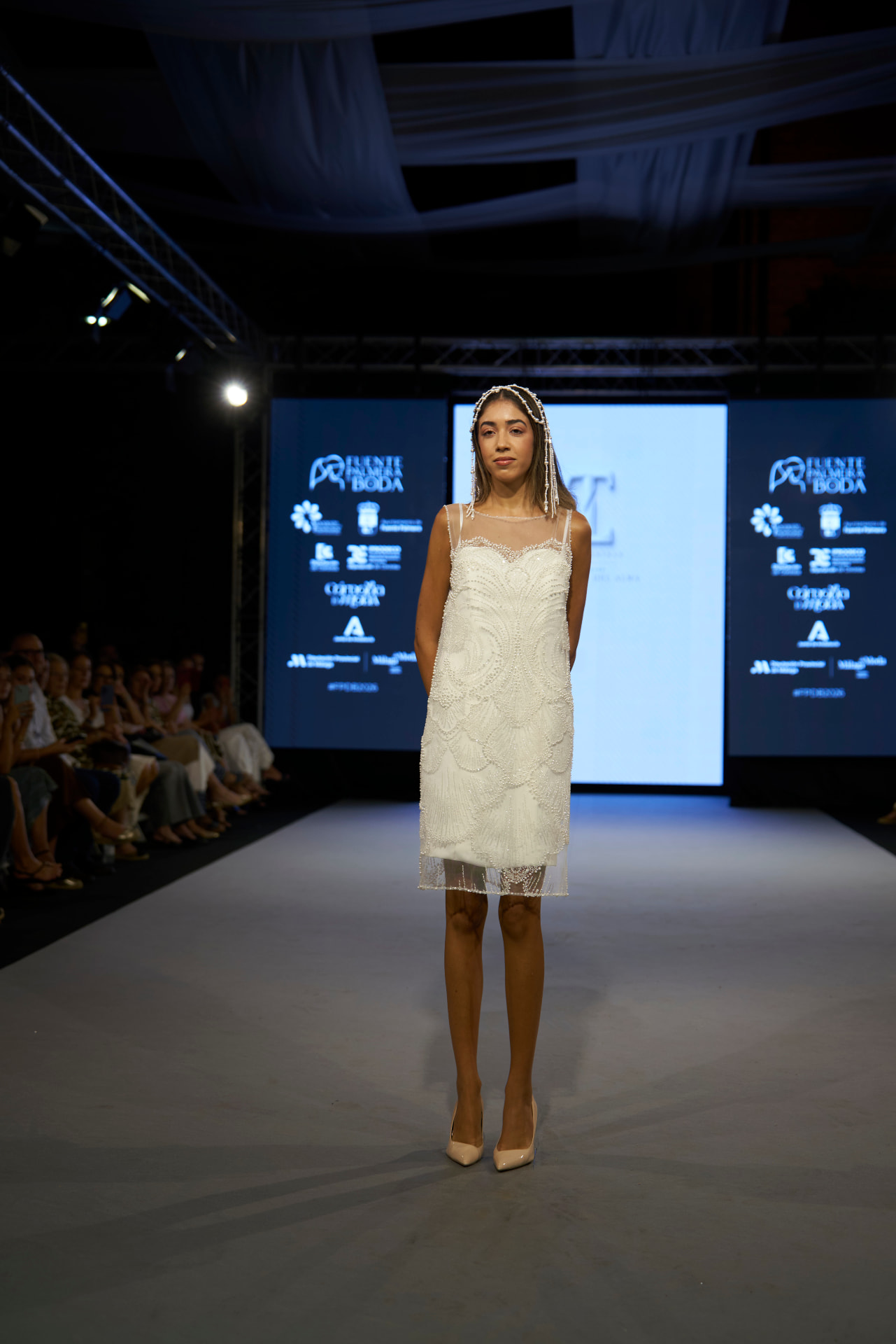 Vestido corto de tul bordado con pedrería y perlas, con tocado de cadenas de perlas, de frente