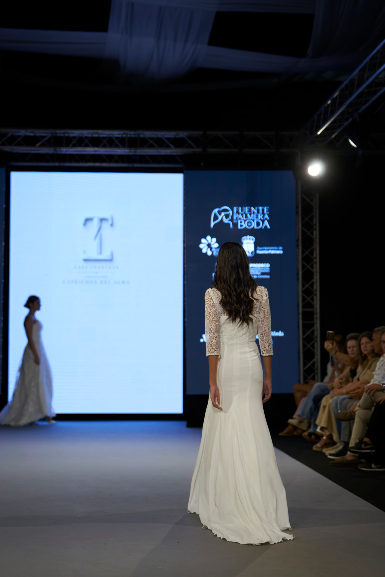 Novia de encaje caminando de espaldas hacia la pantalla de la colección